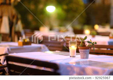 Empty outdoor cafe at dusk. Stylish table decoration with borning candle and natural plant. Empty outdoor cafe at dusk. Stylish table decoration with borning candle and natural plant. 92925067