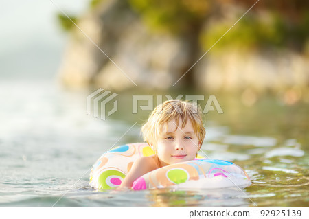 Little boy swimming with colorful floating ring in sea on sunny summer day. Cute child playing on beach. Family and children's resort holiday during summer vacations. 92925139