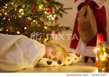 Little boy waiting Santa Claus under tree on Christmas Eve. Child is sleeping. Santa Claus brought gifts. Magic at Christmas and New Year night. Little boy waiting Santa Claus under tree on Christmas Eve. Child is sleeping. Santa Claus brought gifts. Magic at Christmas and New Year night. 92925357