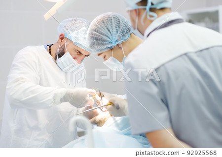 Surgeons and nurse during a dental operation. Anesthetized patient in the operating room. Installation of dental implants in the clinic. 92925568