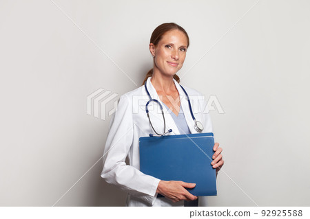 Cheerful young female doctor with stethoscope over neck looking at camera and smiling Cheerful young female doctor with stethoscope over neck looking at camera and smiling 92925588