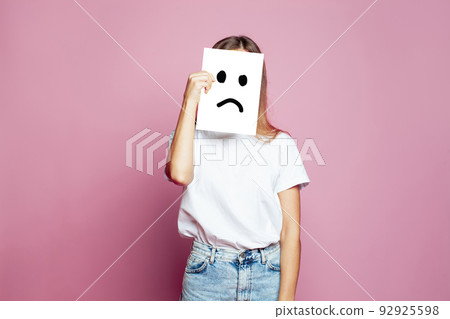 Young woman hiding her face using white paper with sad sign on pink background 92925598
