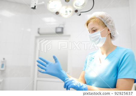 The female surgeon puts on medical protective gloves. Doctor is preparing for surgery in operation room. Medicine and healthcare. The female surgeon puts on medical protective gloves. Doctor is preparing for surgery in operation room. Medicine and healthcare. 92925637