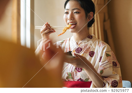 A woman in a yukata eating rice in a room at a travel destination 92925977