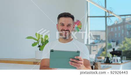 Young successful cafe owner standing in cafe using digital tablet while accepting online order. Coffee shop concept. 92926443