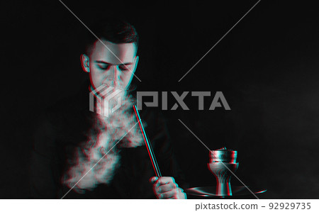 male smoker smokes a hookah and lets out a cloud of smoke male smoker smokes a hookah and lets out a cloud of smoke 92929735