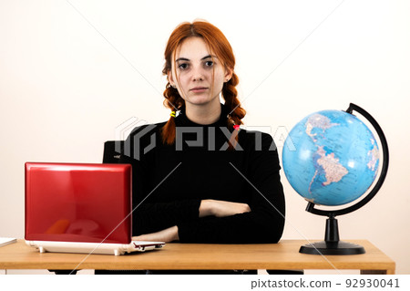 Happy young office worker woman sitting behind working desk with laptop computer, cell phone, notebook and geographic globe of the world. 92930041