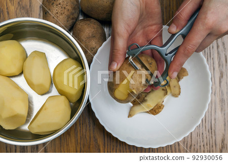 Detail of woman hands peeling fresh yellow potato with kitchen peeler, Food preparation concept. 92930056