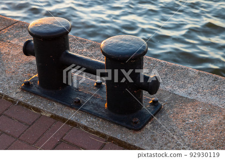 Black coastal bollard is on a concrrete pier, close up 92930119