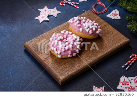 Pink glazed doughnut and marshmallow with Christmas decorations on a wooden cutting board Pink glazed doughnut and marshmallow with Christmas decorations on a wooden cutting board 92930160