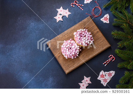 Pink glazed doughnut and marshmallow with Christmas decorations on a wooden cutting board Pink glazed doughnut and marshmallow with Christmas decorations on a wooden cutting board 92930161