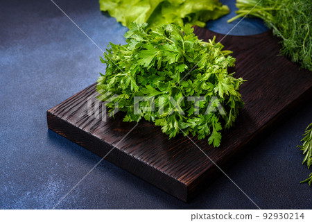 Salad, parsley and dill on a dark cutting board against a blue concrete background Salad, parsley and dill on a dark cutting board against a blue concrete background 92930214