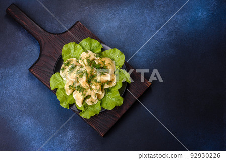 Delicious fresh cooked dumplings with potatoes embellished with greens and lettuce leaves on a dark plate Delicious fresh cooked dumplings with potatoes embellished with greens and lettuce leaves on a dark plate 92930226