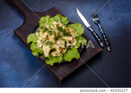 Delicious fresh cooked dumplings with potatoes embellished with greens and lettuce leaves on a dark plate Delicious fresh cooked dumplings with potatoes embellished with greens and lettuce leaves on a dark plate 92930227