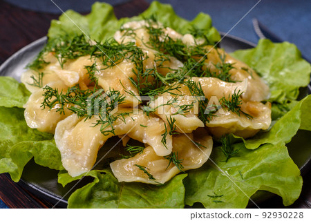 Delicious fresh cooked dumplings with potatoes embellished with greens and lettuce leaves on a dark plate Delicious fresh cooked dumplings with potatoes embellished with greens and lettuce leaves on a dark plate 92930228