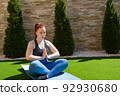 young and beautiful woman, practising meditation in the garden in the open air, relaxation exercises, doing the lotus posture. concept of health and well-being. 92930680