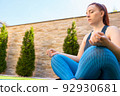 view from below young woman doing yoga, in lotus position, on a mat in the garden. girl doing meditation and breathing exercises. concept of health and well-being. 92930681