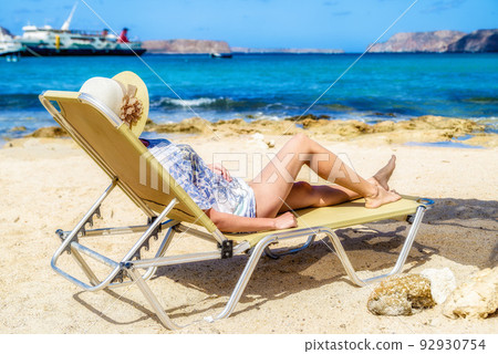 Woman with sunhat lying on the lounger on the beach in exotic tropical resort Woman with sunhat lying on the lounger on the beach in exotic tropical resort 92930754