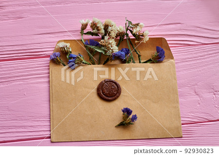 Beige envelope with flowers on pink wooden desk. Attached brown seal. Beige envelope with flowers on pink wooden desk. Attached brown seal. 92930823