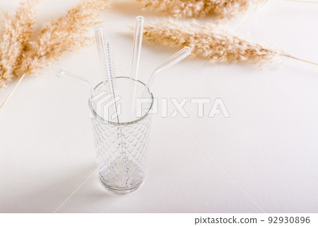 Glass reusable straws for drinks and cleaning brush in a glass on the table. Sustainable lifestyle. Glass reusable straws for drinks and cleaning brush in a glass on the table. Sustainable lifestyle. 92930896