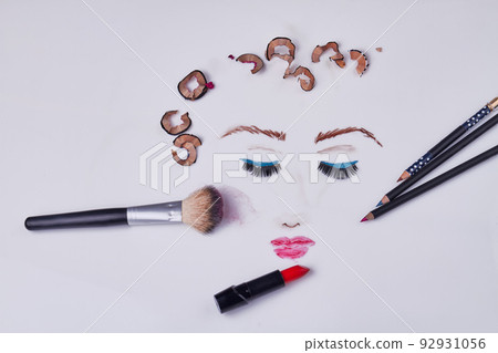 Top view makeup accessories with pencil shavings on white background. Drawn female face with her eyes closed. 92931056