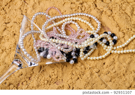 Cocktail glass with pearl necklaces on the sand. Accessories on the beach. Cocktail glass with pearl necklaces on the sand. Accessories on the beach. 92931107