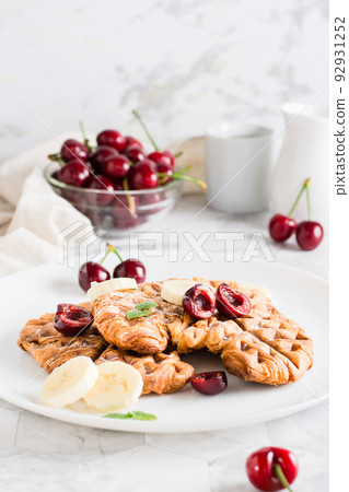 Appetizing croffles with cherries and bananas on a plate on the table. Street food. Vertical view 92931252