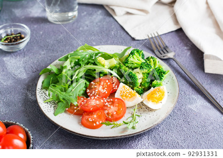 A plate with broccoli, arugula, tomato and boiled egg on a plate on the table. Ketogenic diet 92931331
