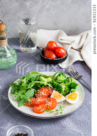 A plate with broccoli, arugula, tomato and boiled egg on a plate on the table. Vertical view 92931333