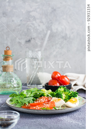 A plate with broccoli, tomato, arugula, boiled egg and sesame seeds on a plate. Vertical view 92931334