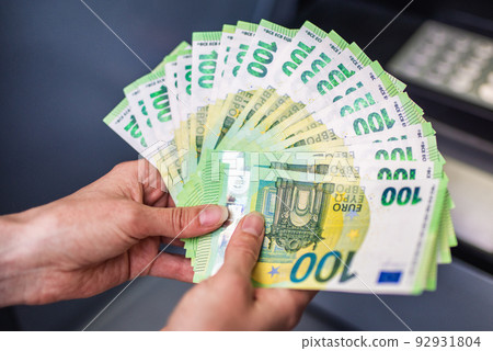 A lot of money in womana lot of money in a woman's hand. Euro banknotes and cach machine in background 92931804
