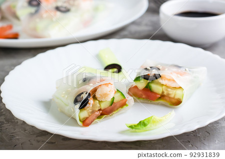 Spring roll cut in half in rice paper with seafood and vegetables on a plate on the table. Close-up Spring roll cut in half in rice paper with seafood and vegetables on a plate on the table. Close-up 92931839