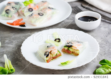 Spring roll cut in half in rice paper with seafood and vegetables on a plate on the table. Homemade oriental cuisine 92931841