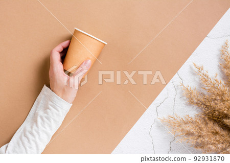 Women's hand holds a disposable cardboard cup for drinks on a two-color background. Eco friendly template. Top view. 92931870
