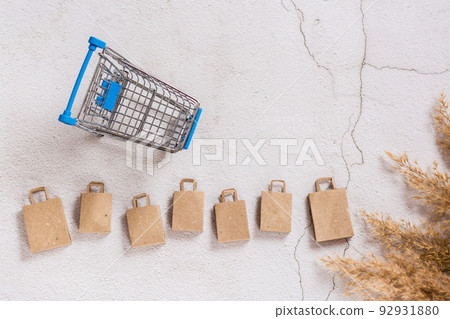 Kraft paper shopping bags in a row and a shopping cart on a concrete background.  Top view. 92931880