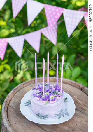 Very beautiful bento cake with purple, veri peri, matthiola flowers with green leaves, candles in the cake on the background of pink flags. Birthday. Vertical photo. Very beautiful bento cake with purple, veri peri, matthiola flowers with green leaves, candles in the cake on the background of pink flags. Birthday. Vertical photo. 92932540