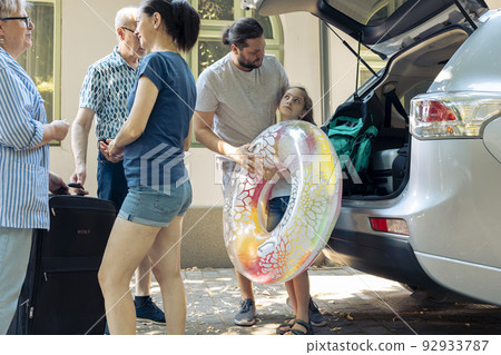 Parents with kid loading bags in trunk, putting baggage in car to leave on holiday vacation journey. Big family with grandparents travelling on summer trip to seaside with inflatable for leisure. 92933787