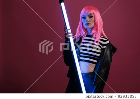 Portrait of sexy woman posing with fluorescent neon light, holding violet purple color lights glowing in dark studio. Wearing rocker leather jacket in front of camera with futuristic lighting. 92933855