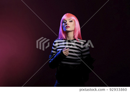 Caucasian attractive woman advertising punk fashion trend in dark shadow light, standing over pink background. Beautiful stylish person wearing leather jacket and pink hair wig in studio. Caucasian attractive woman advertising punk fashion trend in dark shadow light, standing over pink background. Beautiful stylish person wearing leather jacket and pink hair wig in studio. 92933860