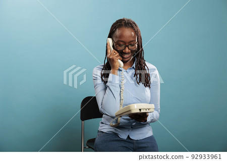 Happy smiling landline telephone operator having a conversation on wired phone on blue background. Confident positive young adult woman answering customer calling for consultancy. 92933961