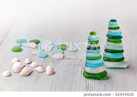 Two pyramid of balanced sea-polished multicolored glass stones on a white wooden deck chair on the beach. 92934026