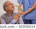 Close up hand of hands of nursing aide holding and patting winkled hand of a patient.Domiciliary care for sick elderly. 92936014