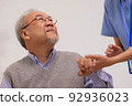 Nursing aide holding and patting winkled hand of a patient.Domiciliary care for sick elderly. 92936023