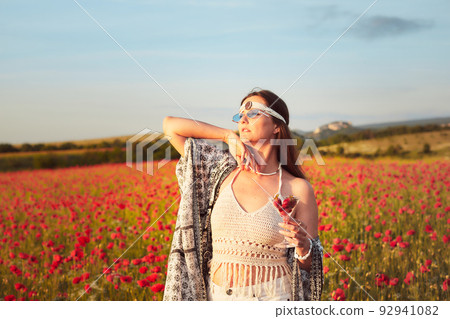 A woman eating strawberries at sunset in a field of poppies. Front view. A woman eating strawberries at sunset in a field of poppies. Front view. 92941082