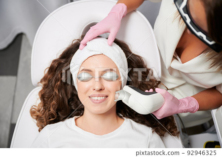 Close-up view laser correction process of vascular asterisks on face in clinic of hardware cosmetology. Doctor working with modern yellow laser for treating vascular defects of face and body. 92946325