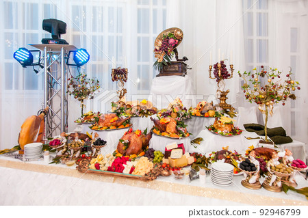 Buffet table with meat snacks, baked pigs in dough, cheese, turkey with fruit, decorated with candelabra and gramophone 92946799