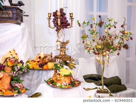 Buffet table with meat snacks, baked pigs in dough, cheese, turkey with fruit, decorated with candelabra and gramophone 92946801