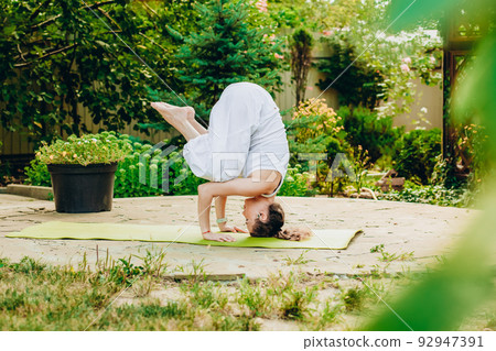 Young woman practices yoga in courtyard of a country house Young woman practices yoga in courtyard of a country house 92947391