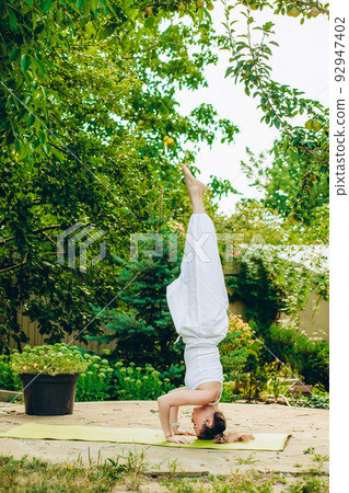 Woman practices yoga in summer garden - Salamba Sirsasana II, Tripod Headstand Woman practices yoga in summer garden - Salamba Sirsasana II, Tripod Headstand 92947402