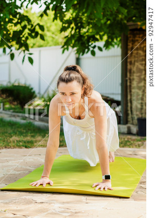 Young woman practices yoga in the garden. Surya namaskar, Plank exercise 92947417